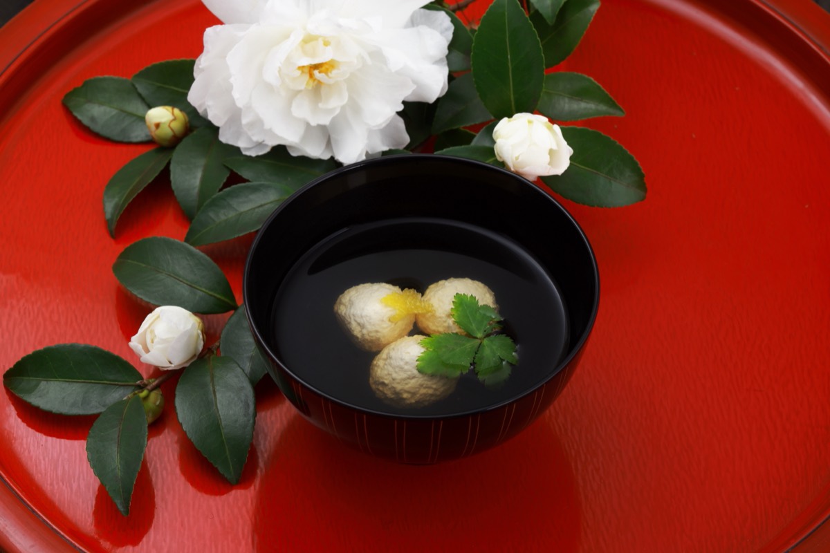 赤い快敷の上の黒椀と、添えられた白い椿の花